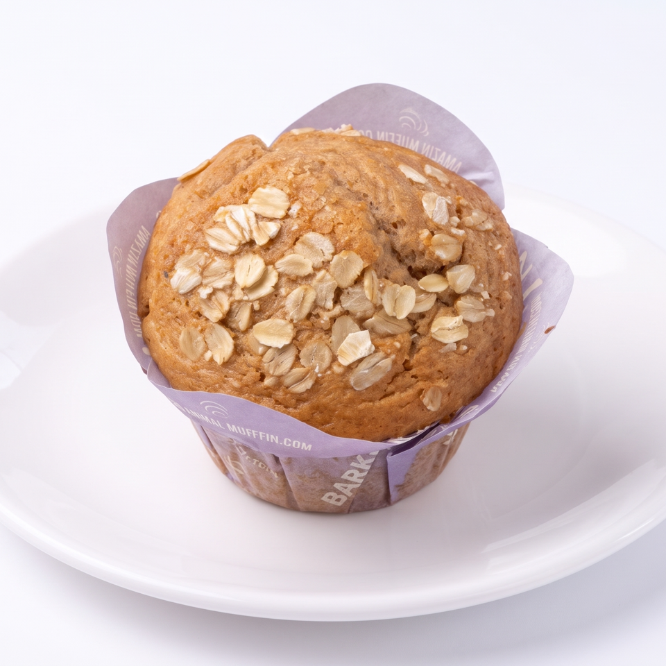Oat-topped muffin in a branded wrapper sits on a white plate against a clean white background.