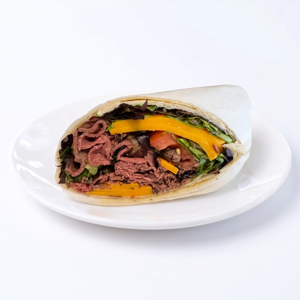 Cross-section of a tortilla wrap filled with sliced roast beef, cheddar cheese, tomatoes, peppers, and mixed greens on a white plate.
