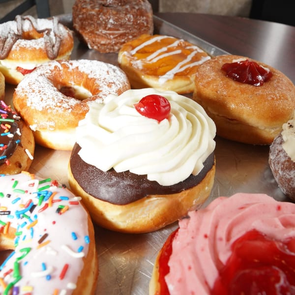 A close-up of various colorful donuts and pastries on a metal tray.