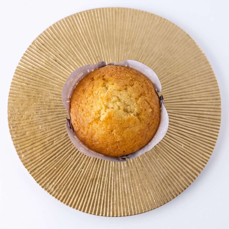 Golden muffin in a branded paper wrapper centered on a textured tan plate.