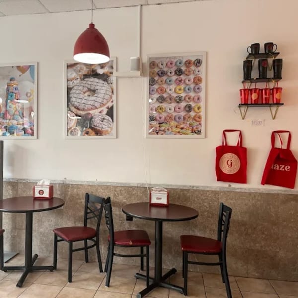 A donut shop interior with two small tables, chairs, donut art, and branded merchandise.
