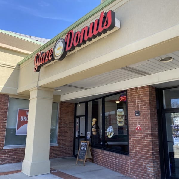 Exterior of Glaze Donuts, a brick and stucco building with a red and black sign.