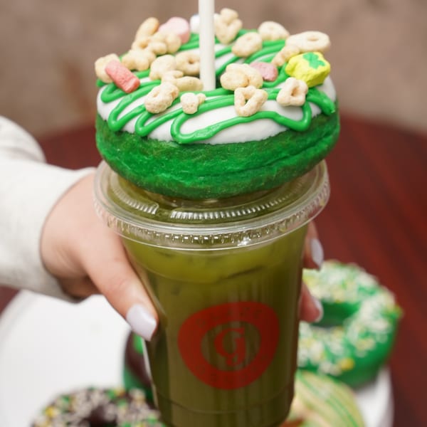 Hand holding a Glaze Donuts matcha drink topped with a green and white frosted donut.