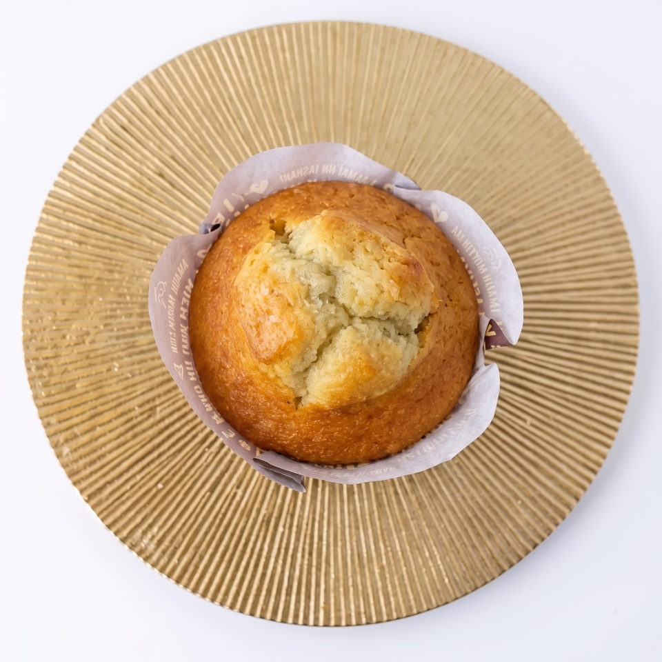 Golden-brown muffin with a cracked, crumbly top in a paper wrapper, centered on a ridged gold plate.