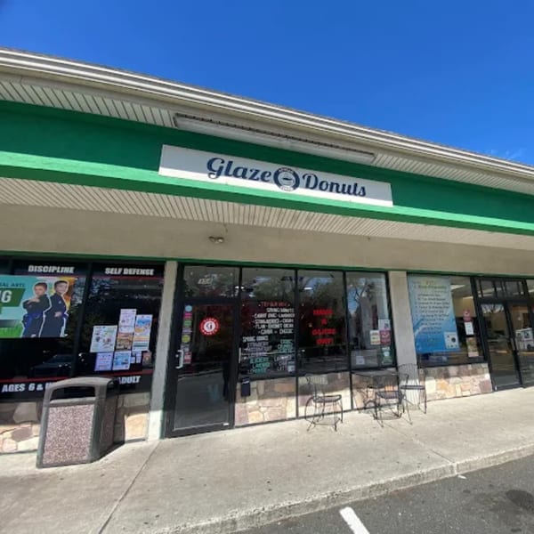 Exterior of Glaze Donuts, a storefront with a green awning, large windows, and outdoor seating.
