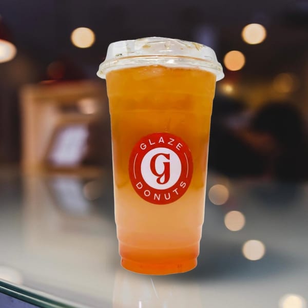 A Glaze Donuts branded cup with a layered orange and yellow drink, against a blurred background.