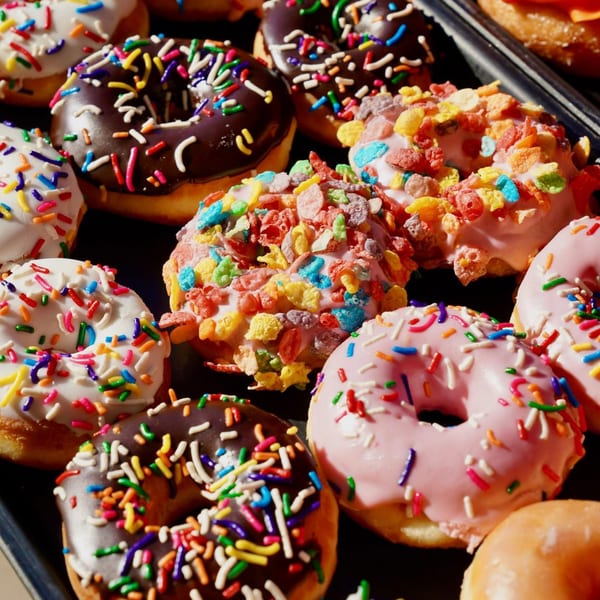 A close-up of various colorful donuts, some with sprinkles, some with cereal, and some with plain frosting.