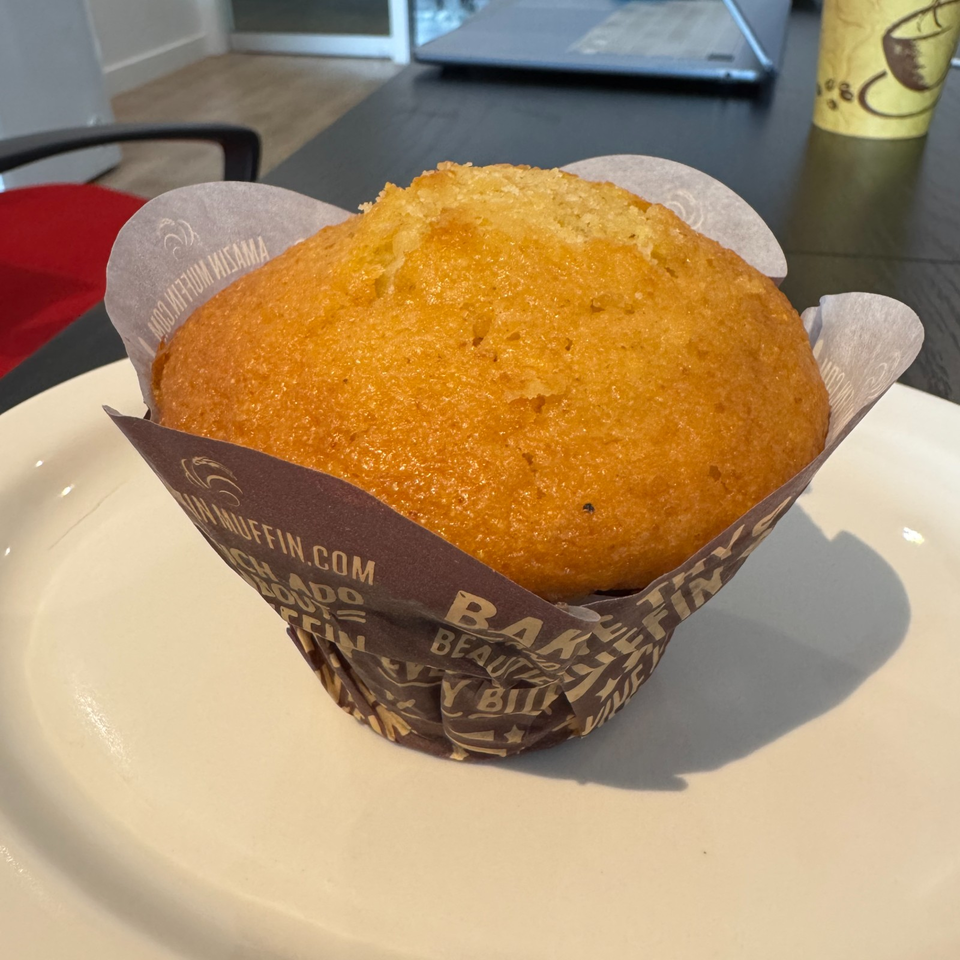 Golden-brown muffin in branded paper wrapping, served on a white plate at a café table.