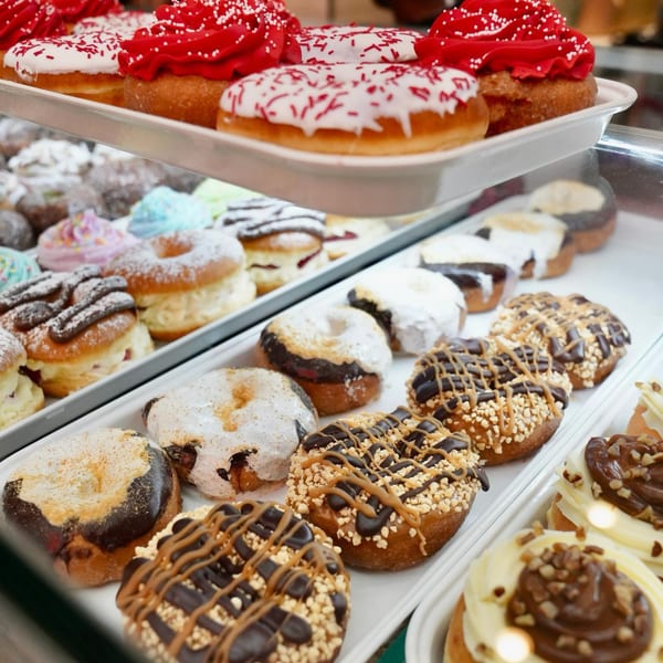A display case filled with various colorful donuts, including red, white, and chocolate frosted varieties.