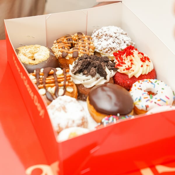 An open red and white box filled with a variety of gourmet donuts with different toppings.