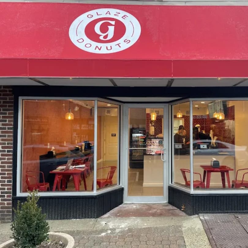 Exterior view of Glaze Donuts storefront with a red awning and visible interior seating.